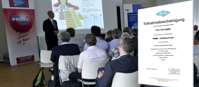 Ein Raum, in dem ein Mann eine PowerPoint-Präsentation auf einem Bildschirm zeigt, während eine Gruppe von Menschen sitzt und zuhört. Im Vordergrund befindet sich auch ein Schild mit deutschem Text.